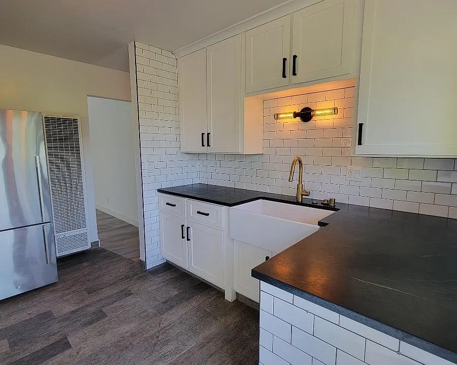 Brass faucet and extra large tub style sink. White ceramic tile and black stone counters