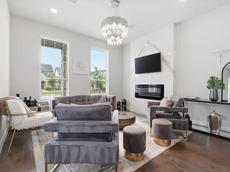 Spacious living area with beautiful wood flooring, with a contemporary fireplace framed with marble accent wall, and an elegant multi-tier crystal chandelier.