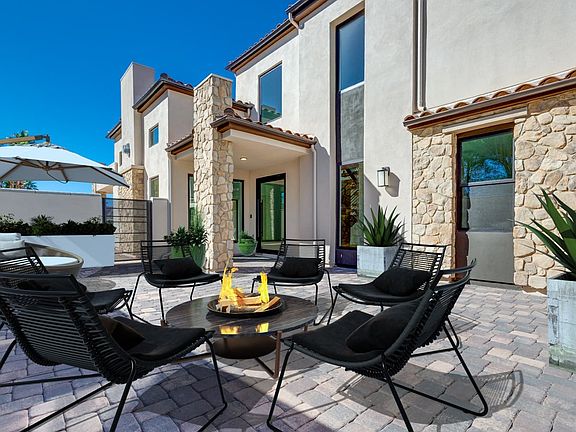 A modern, stone-clad house with a patio featuring a fire pit surrounded by comfortable outdoor furni