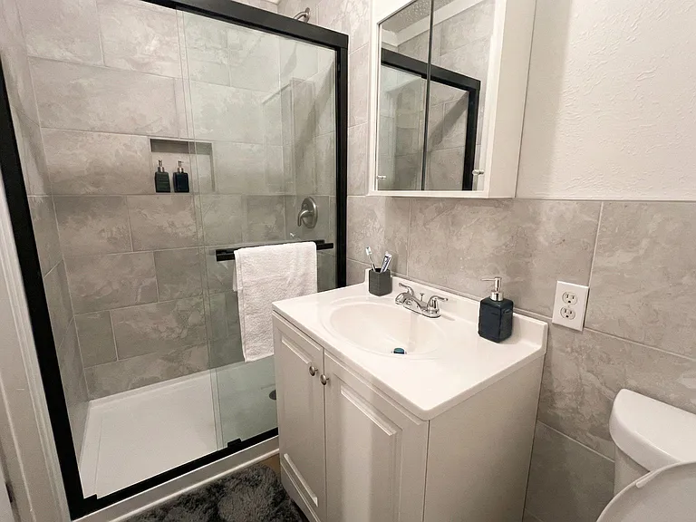 Updated bathroom with tiled tub/shower, glass door, and a vanity with cabinet storage and mirrored medicine cabinet.