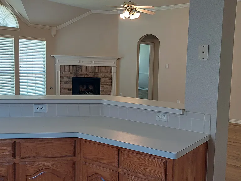 Looking over kitchen counter into living area and archways leading to master bedroom and second archway leading to 2nd, 3rd, and 4th bedrooms, 2nd bath, utility room and garage entrance door. 7/20/2026