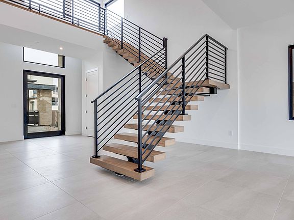 A modern, open-concept entryway with a wooden and metal staircase leading to an upper level, surroun