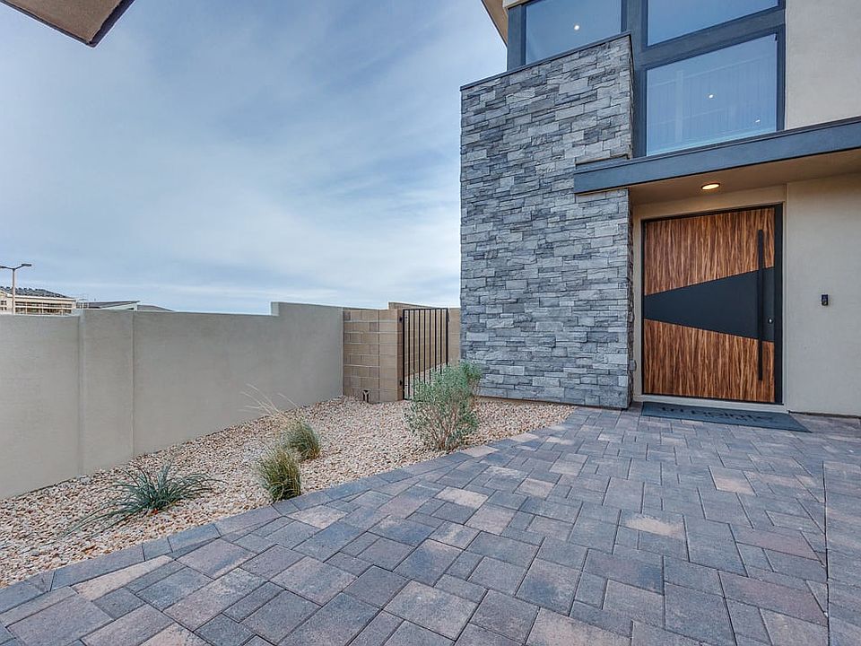 A modern, minimalist exterior with a paved walkway leading to a wooden and glass entrance, surrounde