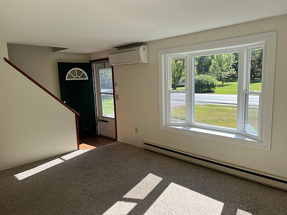Front entrance into living room with bay window, wall-mounted AC/heat, and electric baseboard heat.
