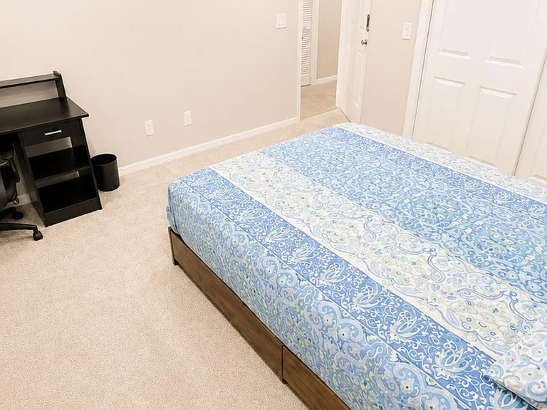 Furnished bedroom with a comfortable bed, dedicated desk workspace, and a spacious closet for everyday storage.