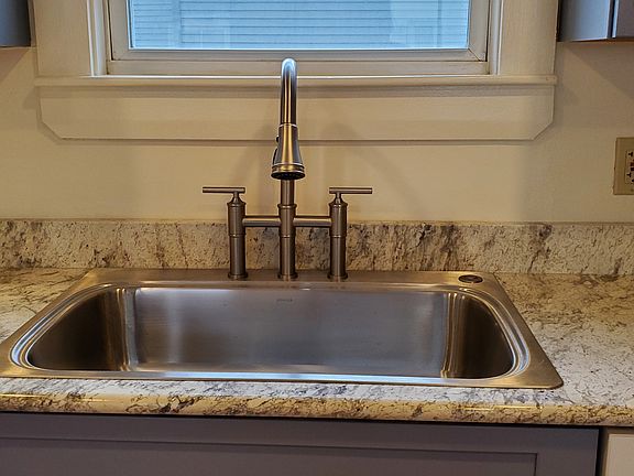 A new deep sink with bridge faucet. A garbage disposal is activated by a button to the right of the faucet