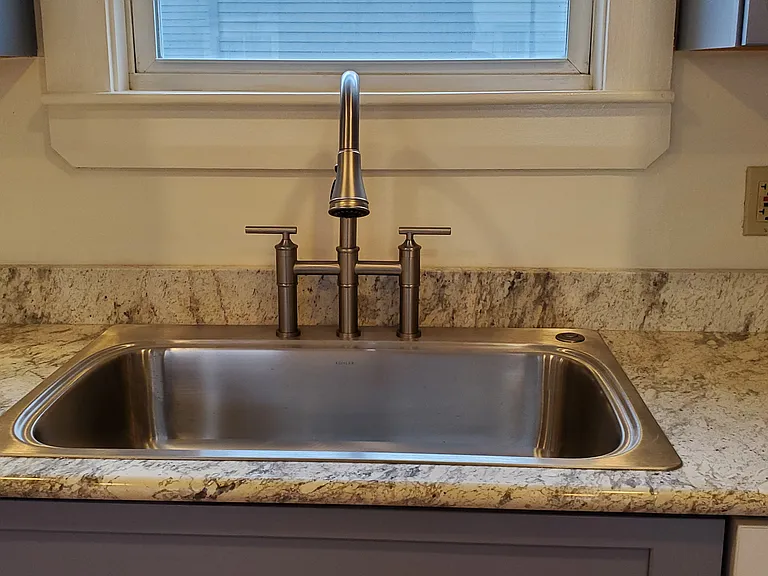 A new deep sink with bridge faucet. A garbage disposal is activated by a button to the right of the faucet