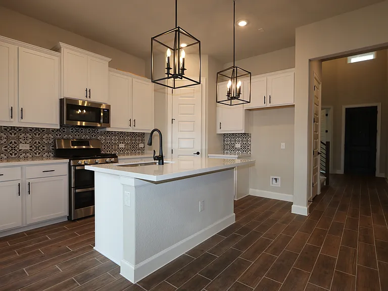 Bright white kitchen with stunning backsplash, brand-new appliances, elegant light fixtures, and abundant storage.