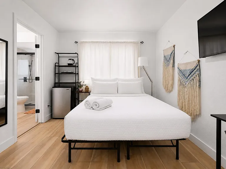 Private bedroom with a queen bed, wall-mounted TV, mini fridge and beverage station, plus an en-suite bath with walk-in showe