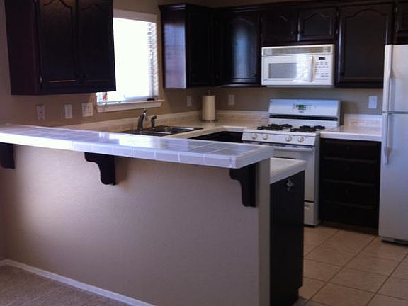 Tiled kitchen with space saver micro, gas range/oven, dw, wrapped in coffee color stain cabinetry. Tiled counters and breakfast bar