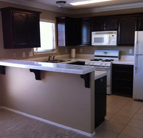 Tiled kitchen with space saver micro, gas range/oven, dw, wrapped in coffee color stain cabinetry. Tiled counters and breakfast bar