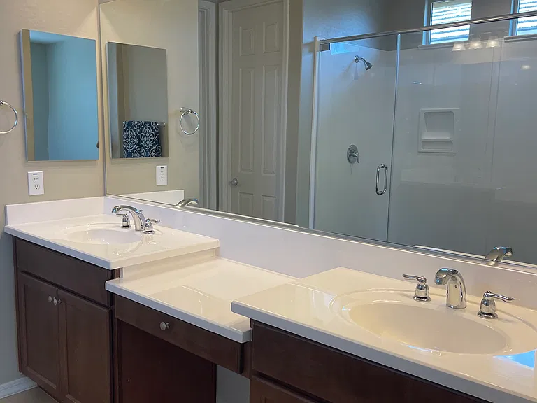Double vanity master bathroom sinks with separate private toilet room. Large double shower noted in reflection of mirror.