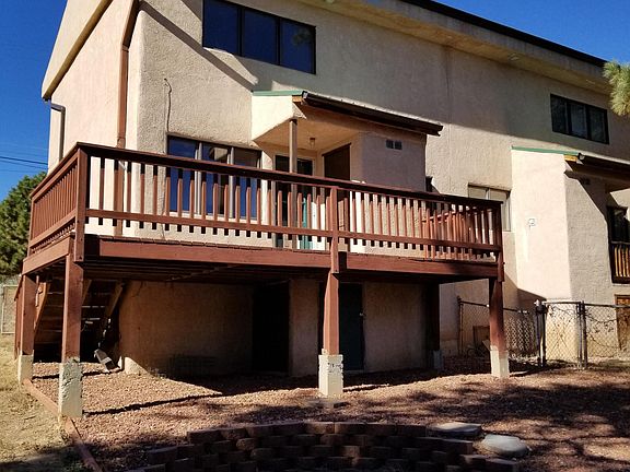 View from fenched backyard showing elevated deck and fire pit area.