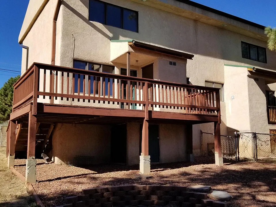 View from fenched backyard showing elevated deck and fire pit area.