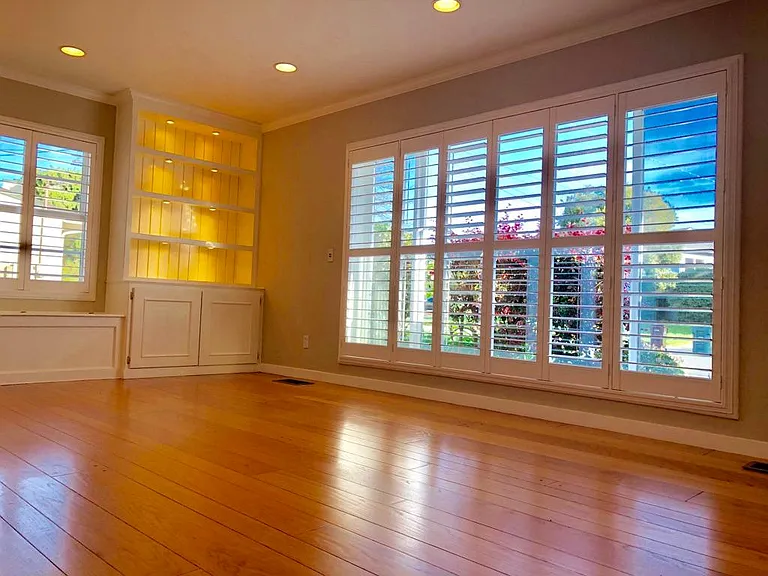 Another shot of living room with picture window to front yard, with plantation shutters