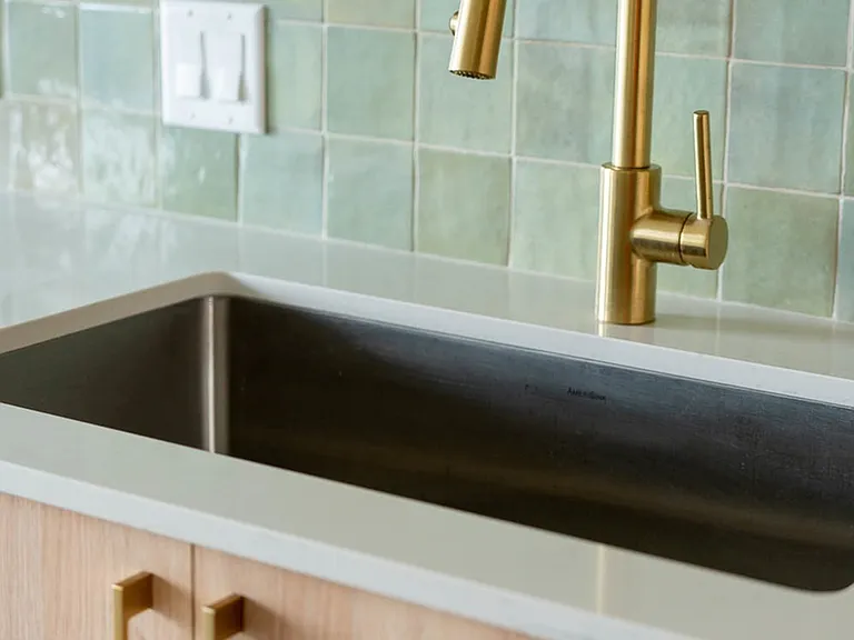 Detail photo of kitchen sink with brass plumbing fixtures.