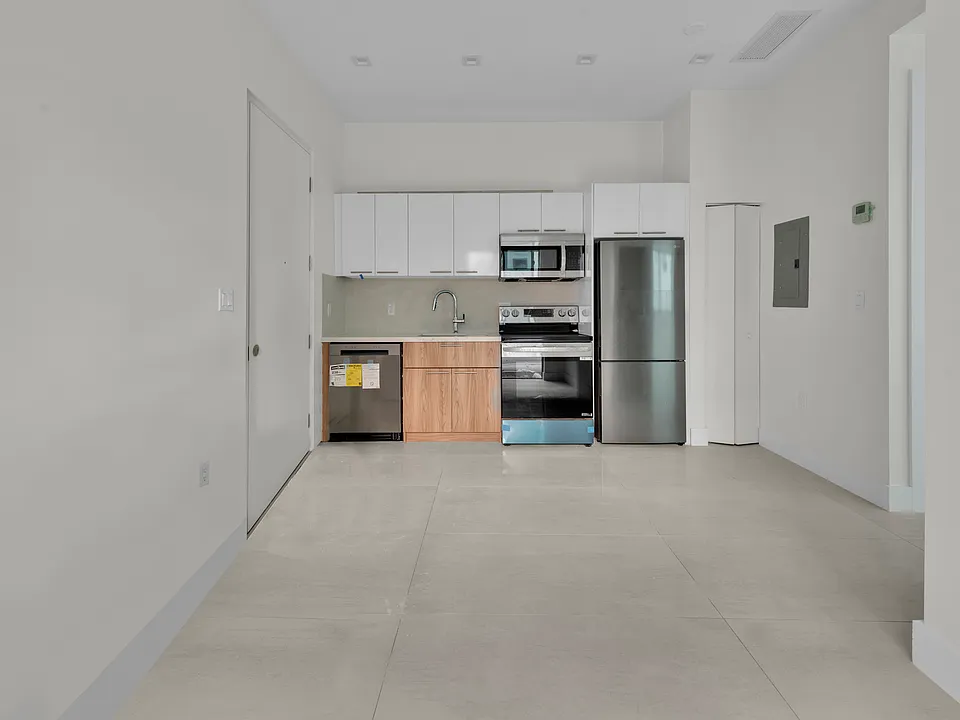 Kitchen with stainless steel appliances and chrome finishes: refrigerator, dishwasher, microwave, and deep sink. View from living area.