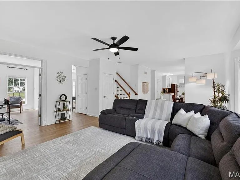 Spacious living area featuring light wood-finish flooring, a contemporary ceiling fan, and crisp white walls