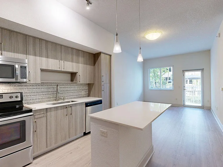 Apartment kitchen with stainless steel appliances, light counters, and wood style floor.