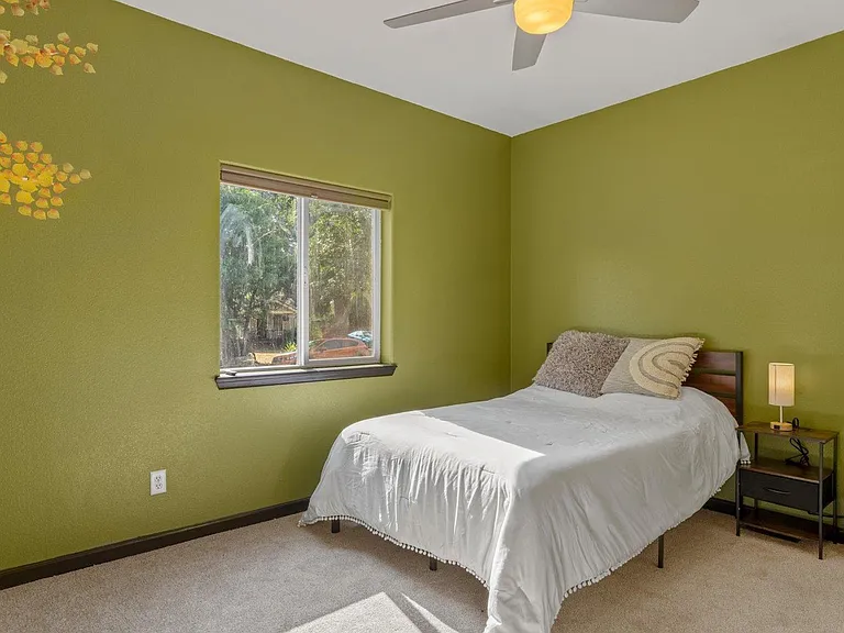 Furnished bedroom with a twin bed, nightstand, ceiling fan, and window overlooking greenery for natural light.