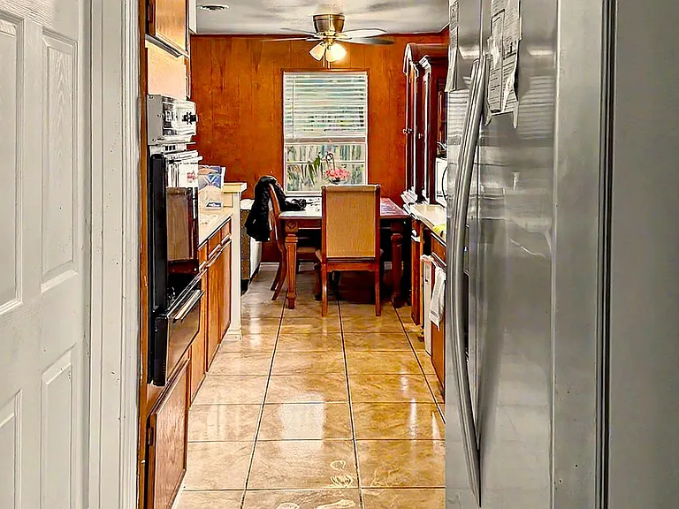 Galley kitchen with ample wood cabinetry, full-size appliances, and a tiled floor leading to an eat-in dining nook.