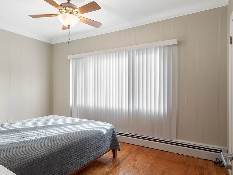 Primary bedroom featuring hardwood floors, a ceiling fan, crown molding, and a large window with vertical blinds.