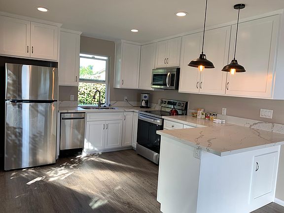 Spacious bright kitchen with quartz countertops, stainless steel appliances, breakfast bar, and vintage lights