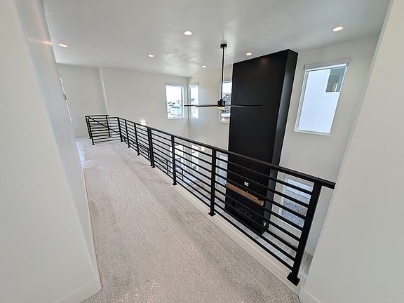 A modern interior loft with black metal railing overlooks a living area below. The space has white w