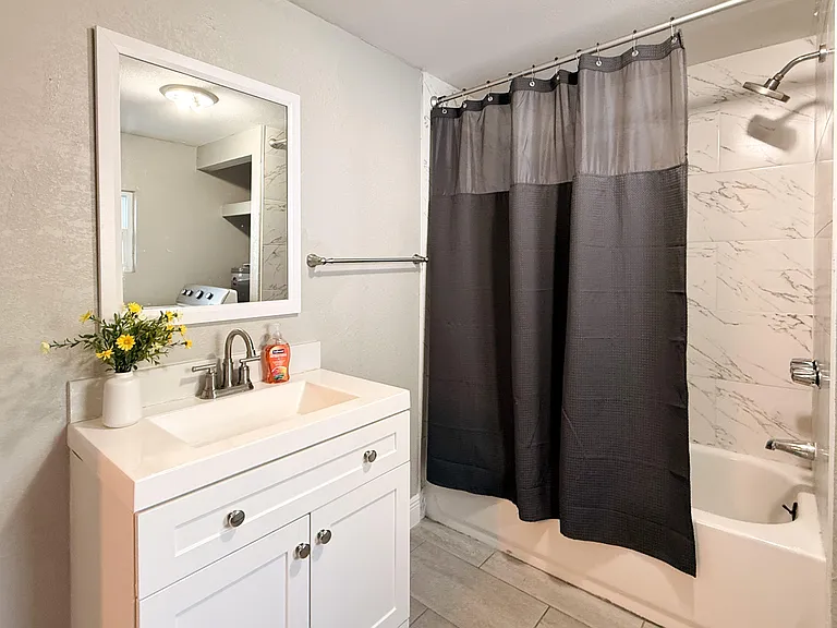 Full bathroom with single-sink vanity, framed mirror, and tub/shower combo with tile-look surround.