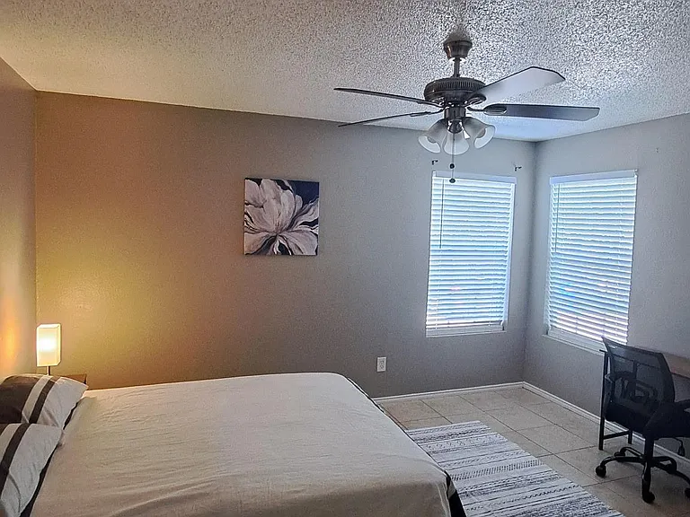Spacious bedroom with a ceiling fan, dual windows with blinds, and a dedicated desk area for work or study.