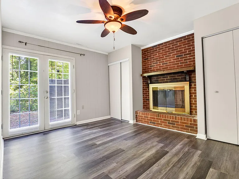 Open living area with durable plank flooring, ceiling fan, and brick fireplace, plus glass doors leading to an outdoor space.