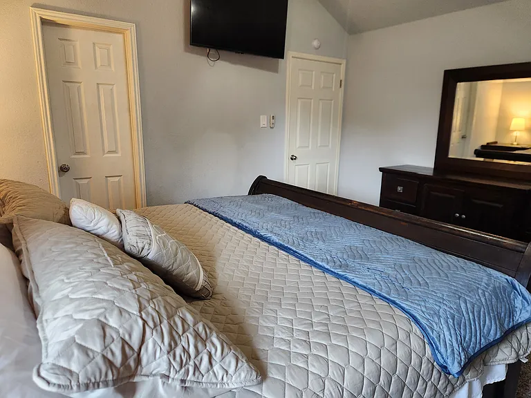 Primary suite features King bed, dresser, nightstands, mirror, TV and en suite bathroom w/ walk in closet. Private door to back patio and window.