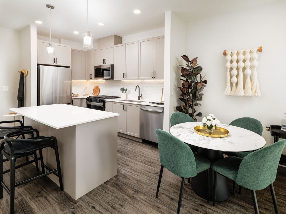 Kitchen and dining area with grey cabinetry, white quartz countertops, white tile backsplash, stainless steel appliances, and pendant lighting