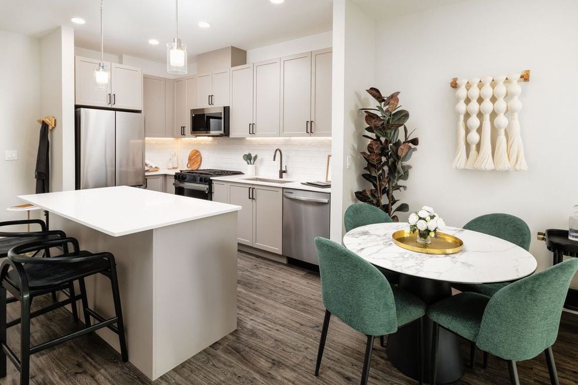 Kitchen and dining area with grey cabinetry, white quartz countertops, white tile backsplash, stainless steel appliances, and pendant lighting