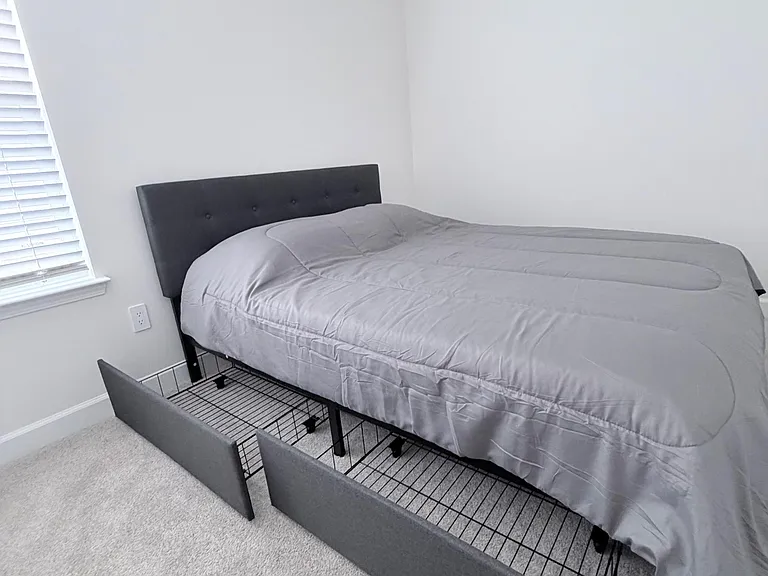 Furnished bedroom with a full bed, plush carpet, and a window with blinds for light and privacy.