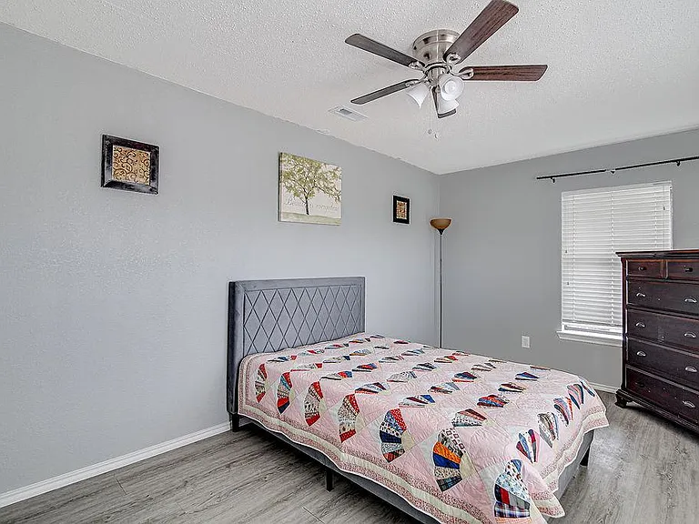 Bedroom features a comfortable sleeping area, ceiling fan, and a window with blinds plus dresser storage space.