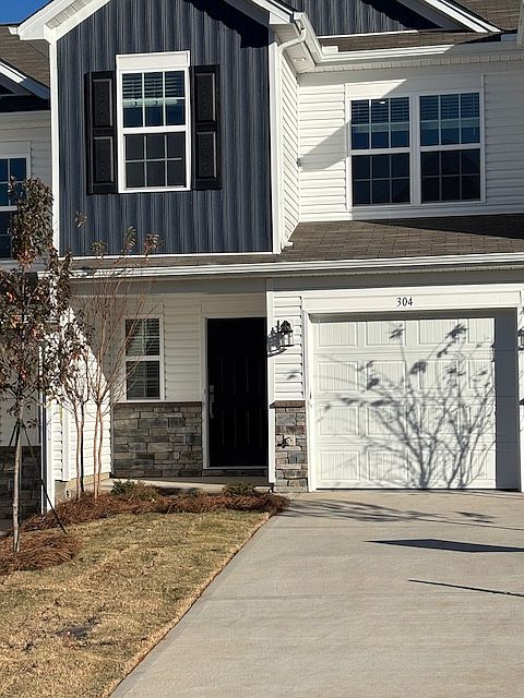Front entrance with blue siding and stone facade. 1-car garage and parking for another vehicle in driveway.