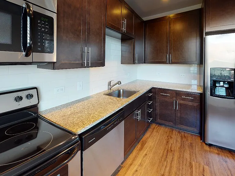 Apartment kitchen with stainless steel appliances, granite countertops and wood-style flooring.
