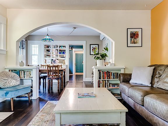 Living room features beautiful arch-way, hard wood floors, white brick fireplace with wood stove, fresh paint (2023) and beautiful built-in bookshelves.