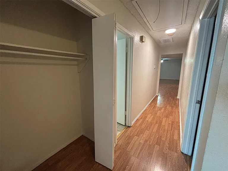 Hallway featuring wood-finish flooring, light neutral wall paint, and a built-in closet with shelving
