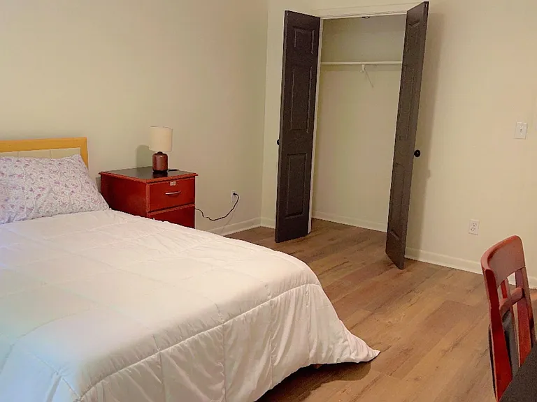 Furnished bedroom with a full bed, nightstand and lamp, hardwood-style floors, and an open closet for easy storage.