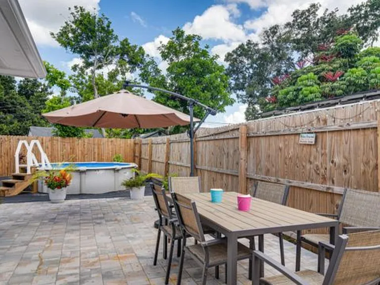 Fenced paver patio with outdoor dining set, shade umbrella, and an above-ground pool for relaxing and entertaining.