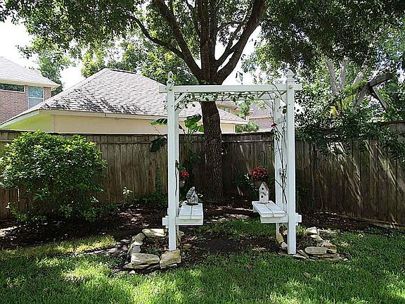 The gazebo has built-in benches and is under a shade tree.