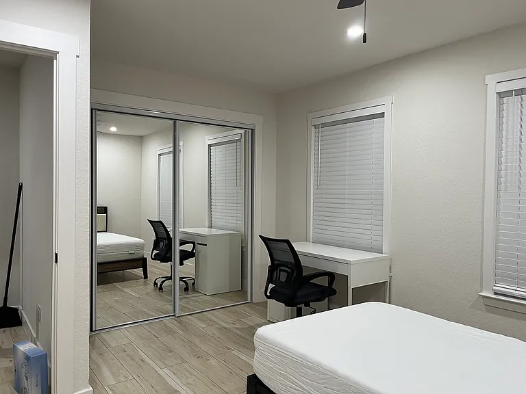 Primary bedroom with large mirrored door wall closet. Primary bedroom furnished with TwinXL bed, tall dresser, desk, and chair.