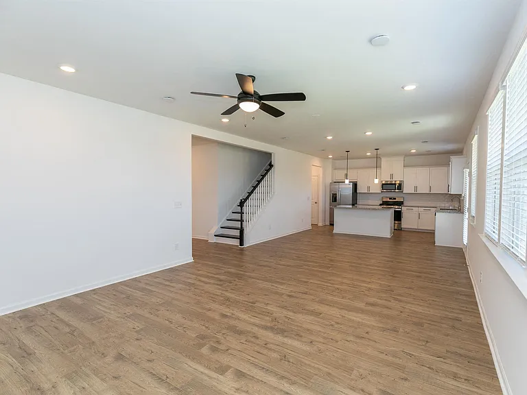 Living room with ample amount of space with wood floors and a ceiling fan.