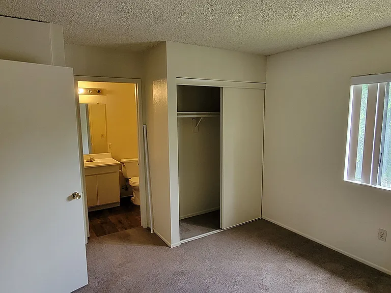 Carpeted bedroom with large window and private bathroom at Magnolia Apartments in Riverside, California.