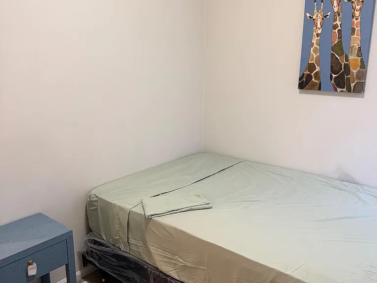 Furnished bedroom with a comfortable bed, carpet flooring, and a handy nightstand for everyday essentials.