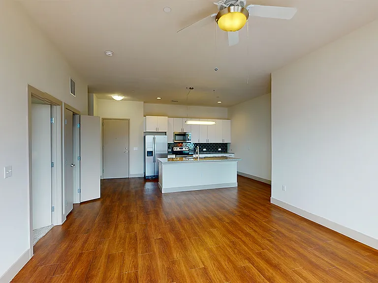 Apartment kitchen with stainless steel appliances, dining and living room with wood-style flooring.