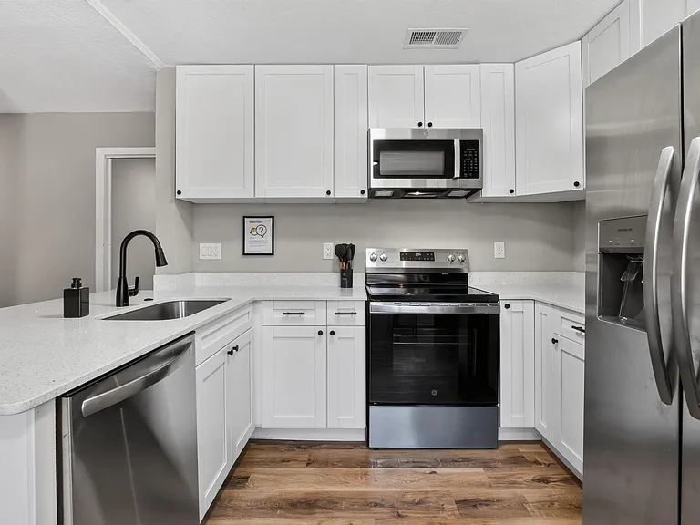 Updated kitchen with ample white cabinetry, generous counters, and stainless steel appliances including dishwasher and fridge