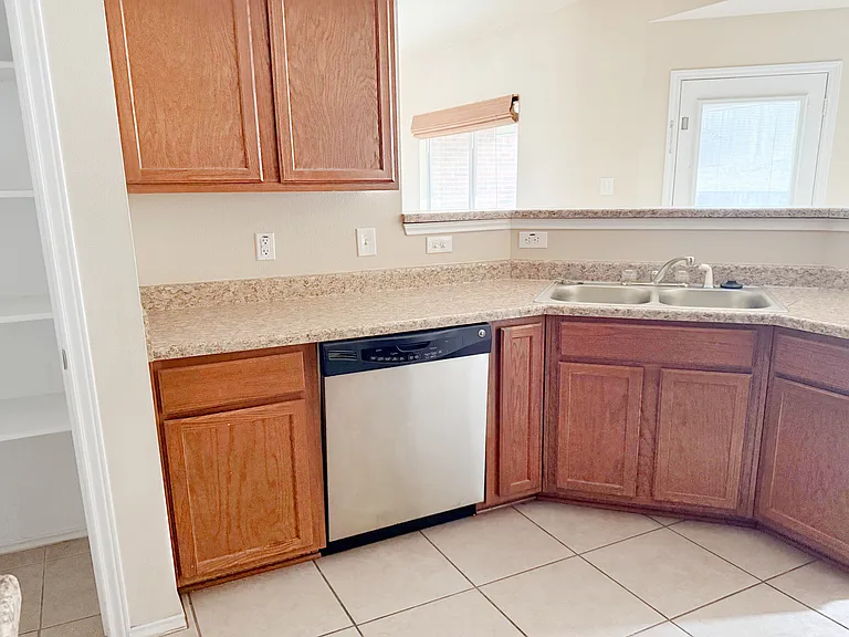 Kitchen with stainless steel dishwasher, double sinks & more cabinets.